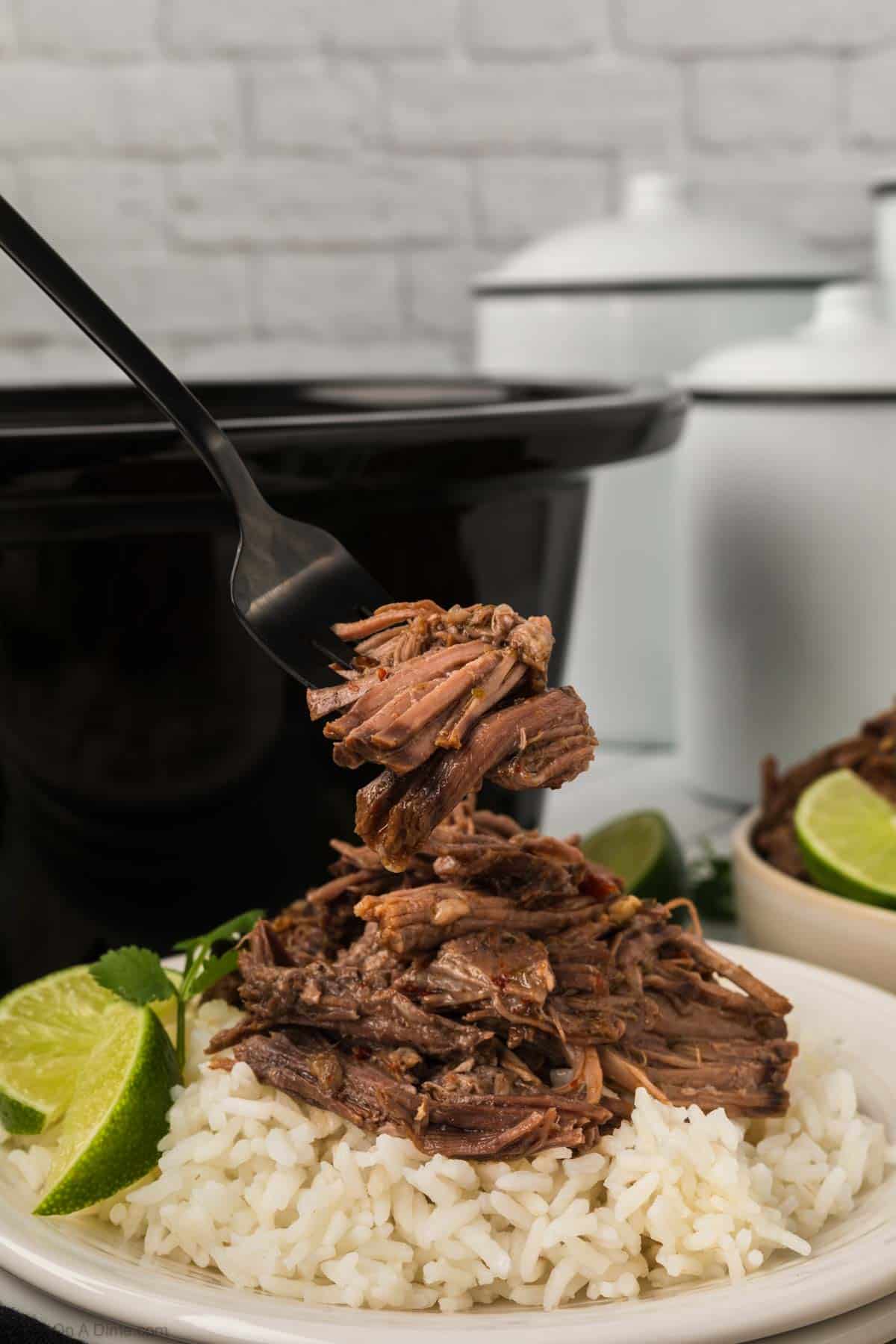 Shredded beef on white rice on a plate with fresh lime wedges