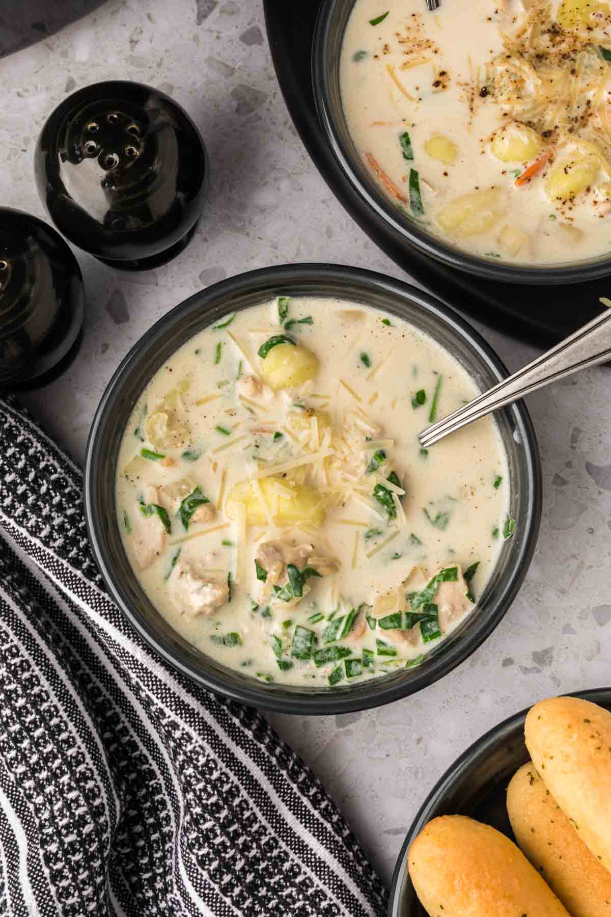 Close up image of Chicken Gnocchi Soup in a black bowl with a spoon and breadsticks on the side