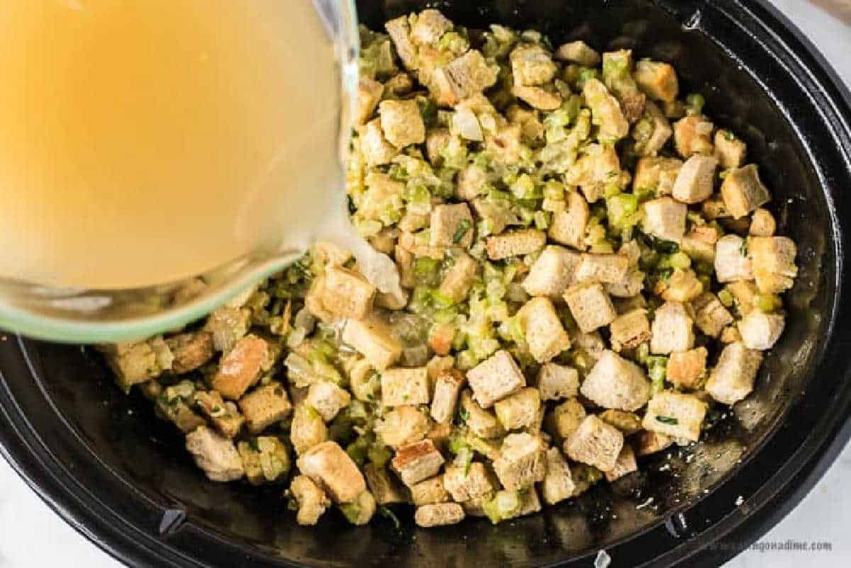 Placing the dry bread crumb mixture in the slow cooker and pouring the chicken broth in.