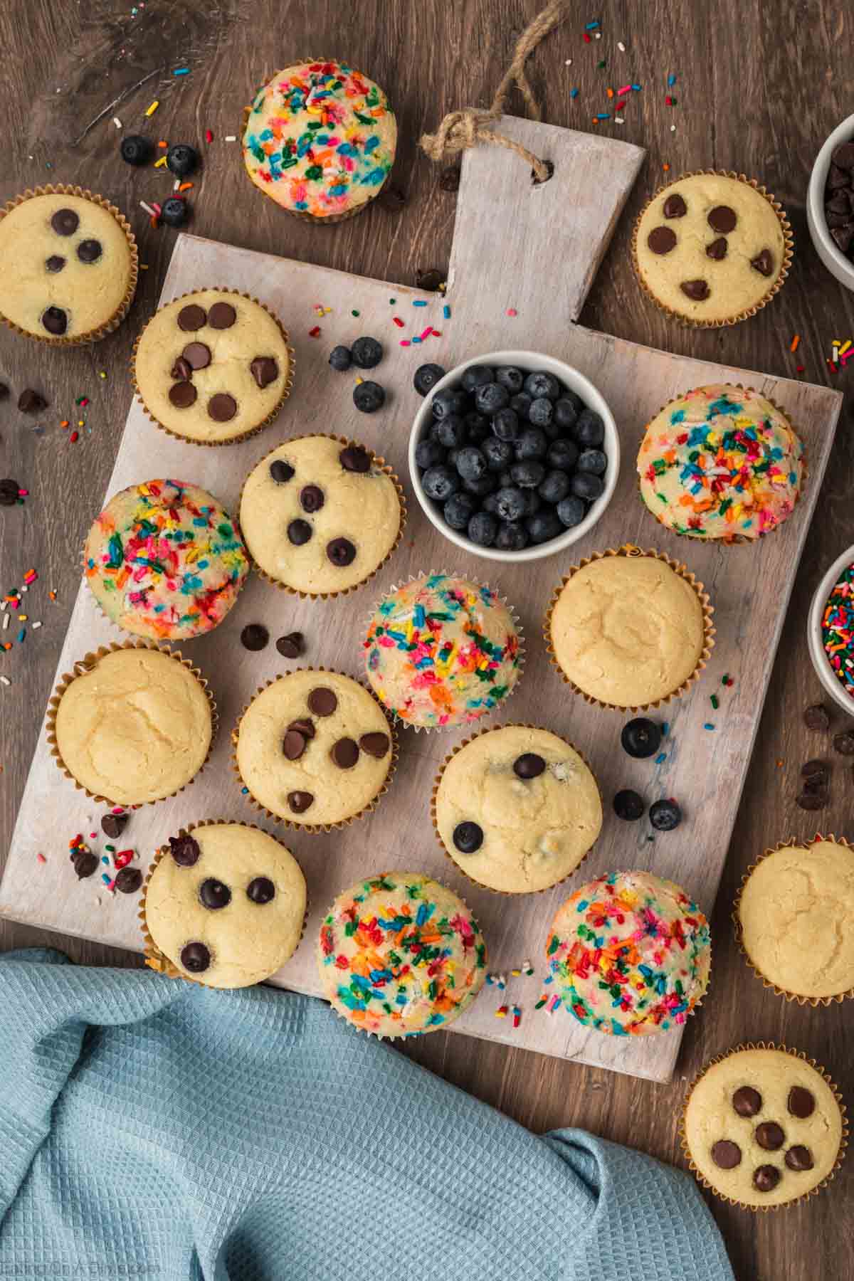Pancake Muffins on a wooden platter. There are muffins with chocolate chips and sprinkles with a bowl of blueberries
