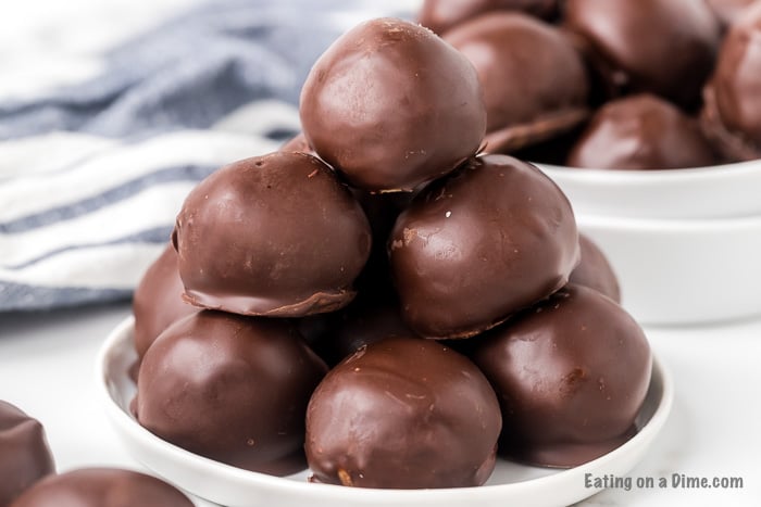 Chocolate covered peanut butter balls stacked on top of each other with a ball of peanut butter balls behind it. 