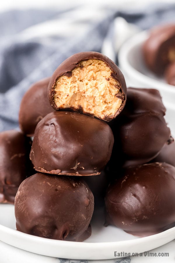 Chocolate covered peanut butter balls stacked on top of each other with a bite taken out of one of the balls with a blue linen behind it. 