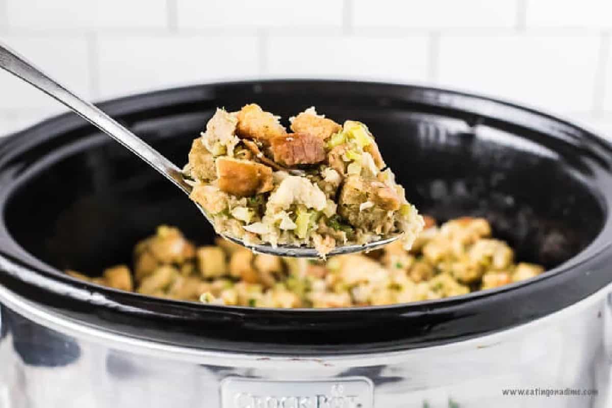 Crockpot stuffing recipe is so simple to make and will be everyone's favorite side dish during the holidays. The slow cooker does all of the work and makes this stuffing recipe easy! Home made bread stuffing is simple and the best for Christmas and more. #eatingonadime #crockpotstuffing #recipeseasy #crockpot #homemade Stuffing in the crock pot with a serving on a spoon.