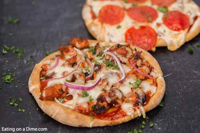 A BBQ Chicken Pita Pizza on a black platter with a pepperoni pizza behind it. 