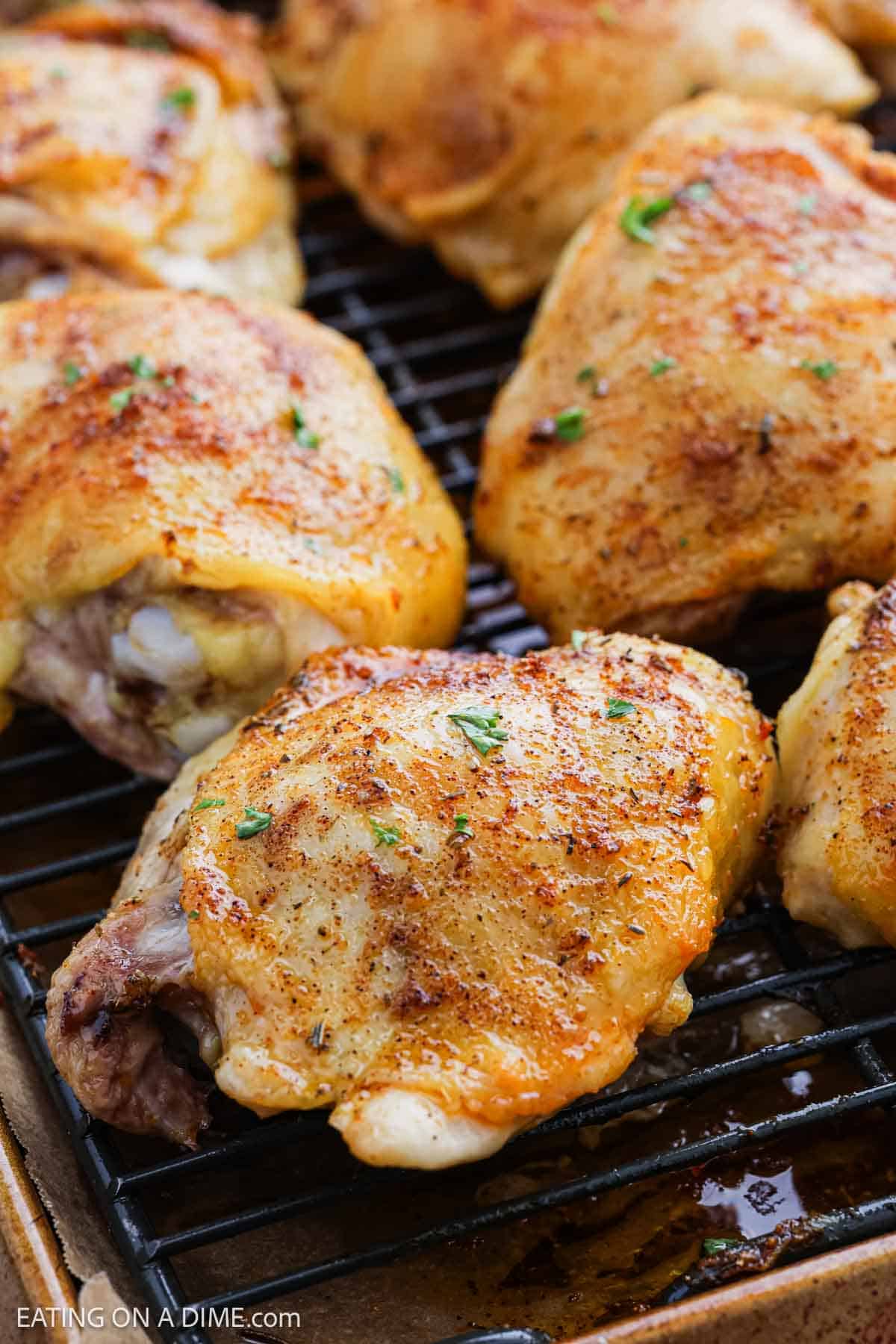 Close-up of golden-brown Oven Baked Chicken Thighs on a wire rack, perfectly seasoned with herbs and spices and resting on a baking sheet.