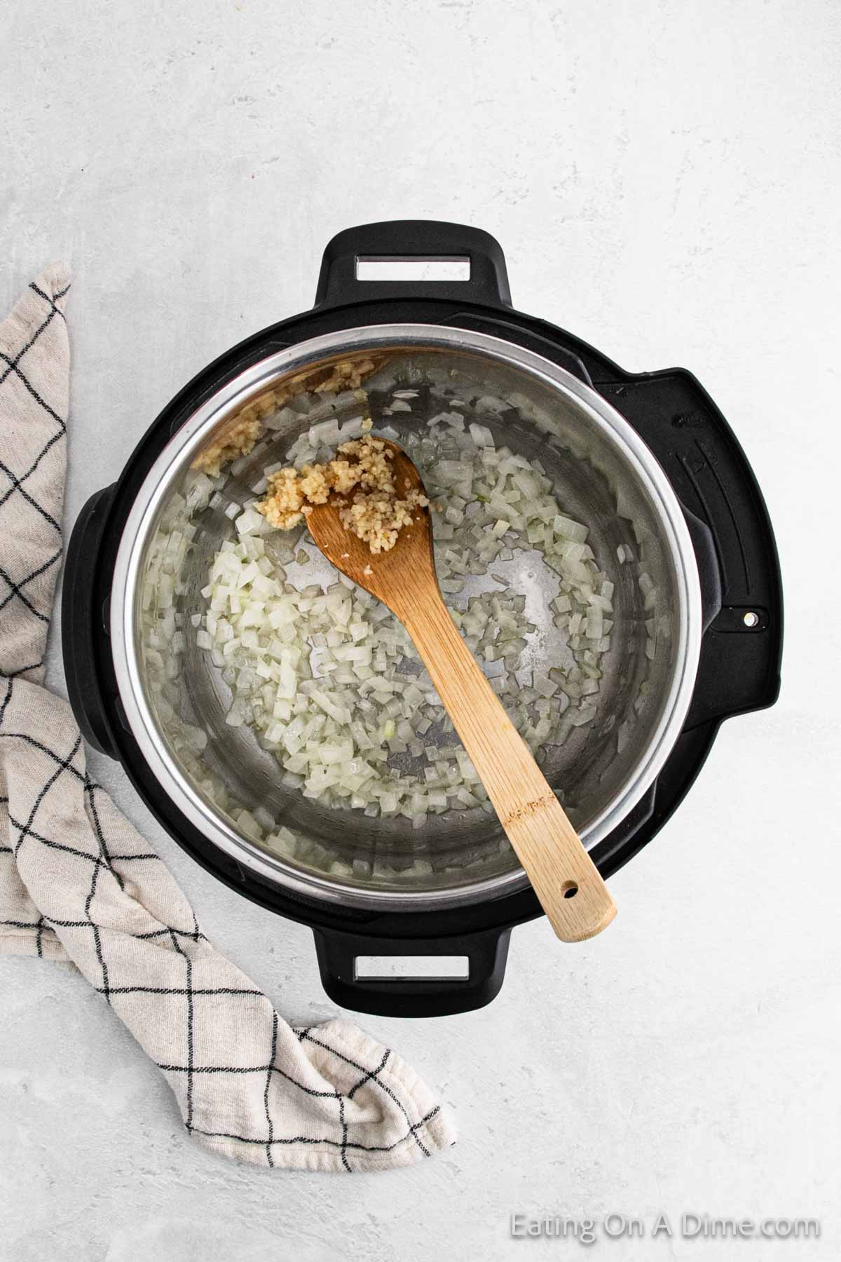 Minced garlic mixed with cooked chopped onions in the instant pot with a wooden spoon
