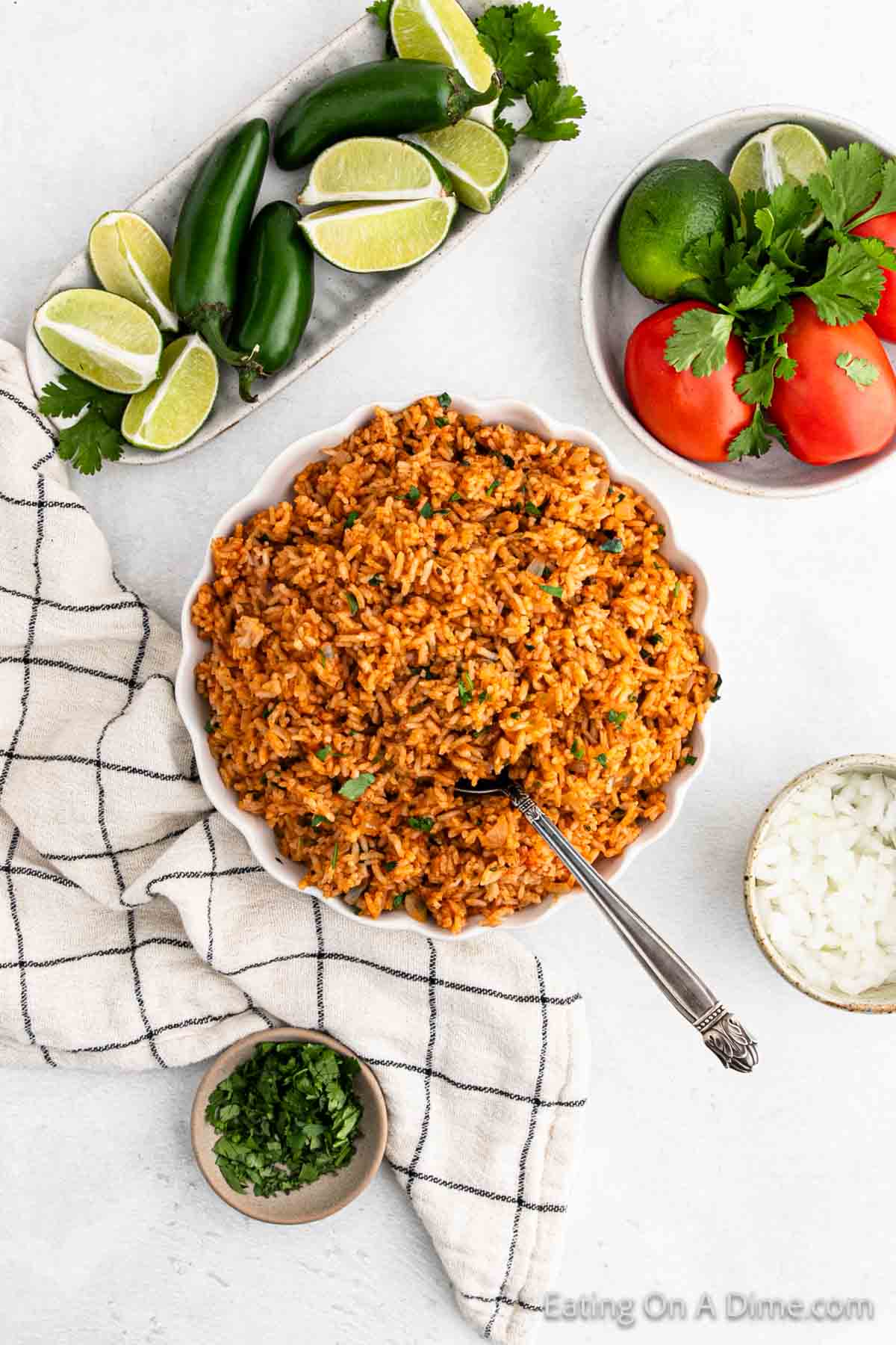 Spanish Rice in a bowl with a platter of Jalapeno and fresh lime wedges and a bowl of tomatoes on the side
