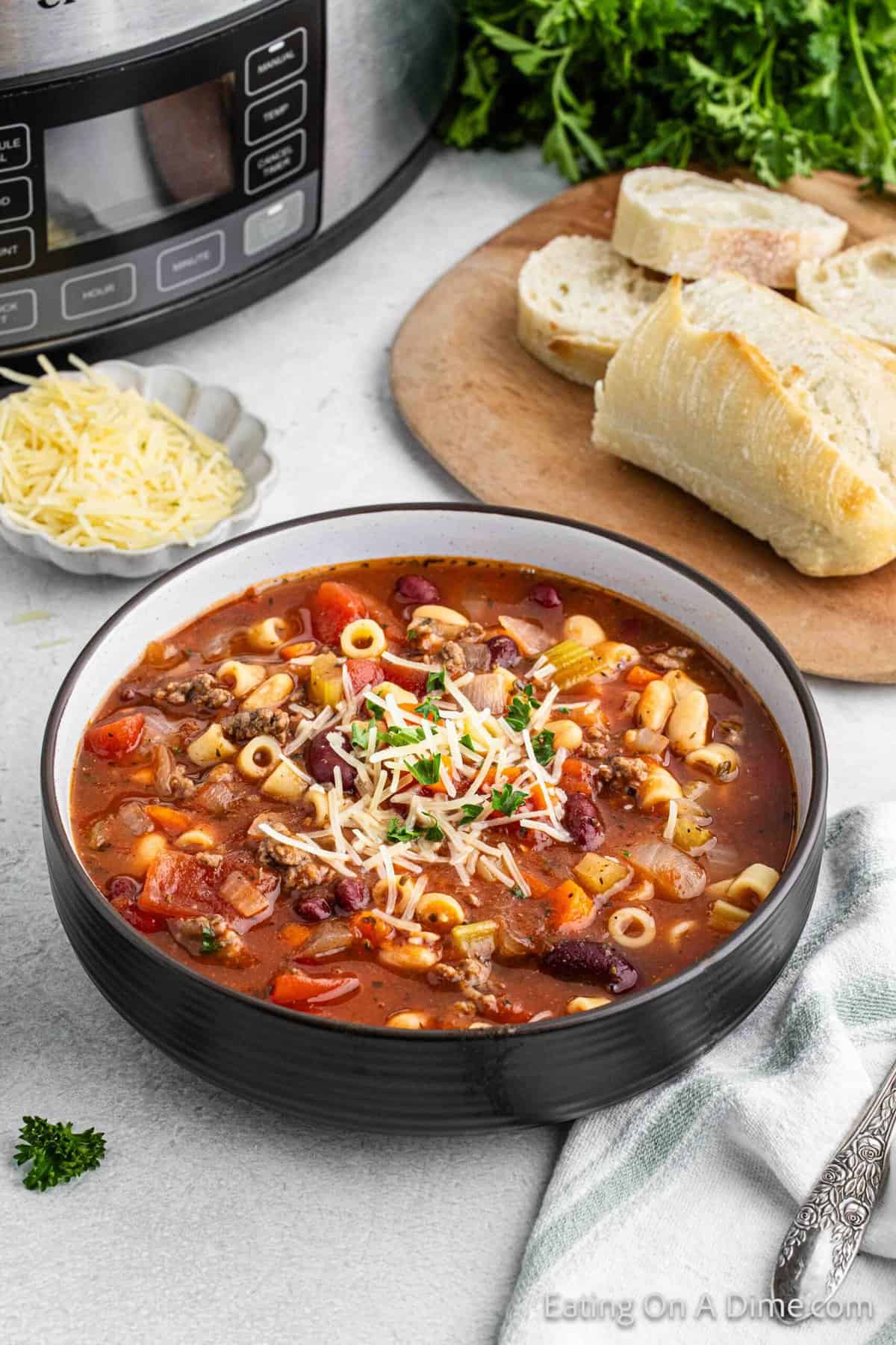 Pasta Fagioli in a bowl topped with shredded parmesan cheese and french bread on the background