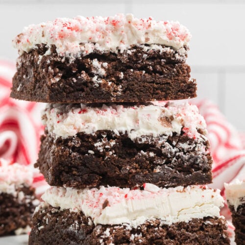 A stack of peppermint brownies with white frosting, with faded peppermints in the background.
