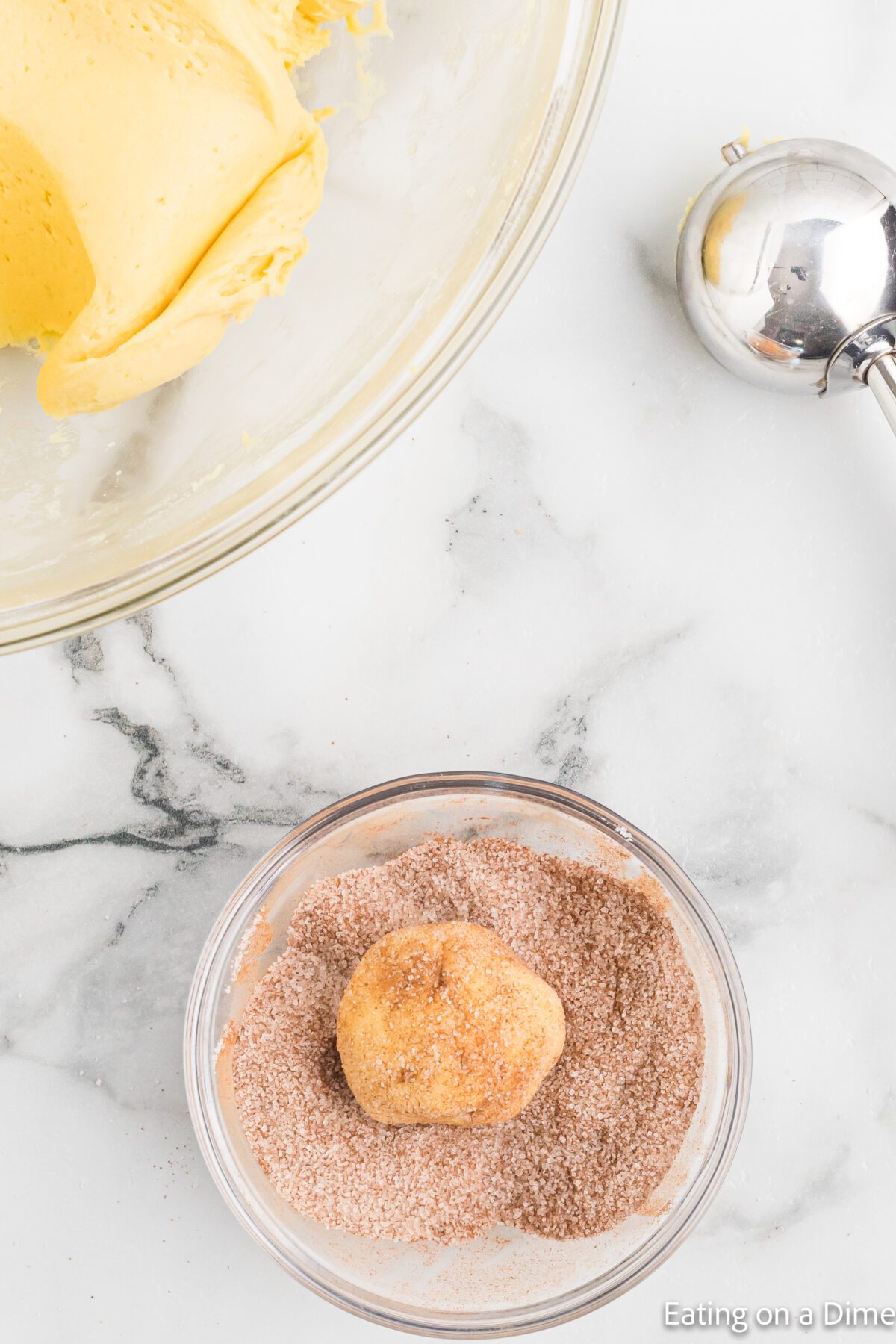 Snickerdoodle balls rolling into cinnamon and sugar bowl