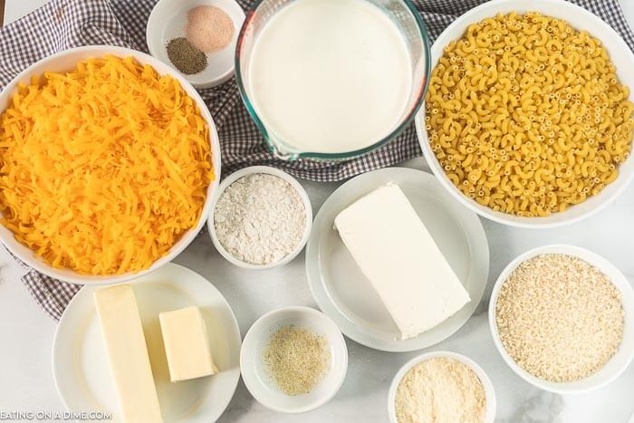 Close up image of Ingredients for Baked Mac and Cheese. Pasta, butter, flour, milk, heavy cream, cheddar cheese, cream cheese salt and pepper, bread crumbs, parmesan cheese garlic salt. 