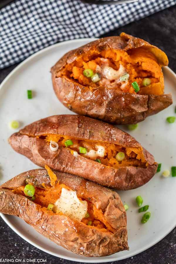 Cooked Sweet Potatoes on a white plate topped with butter and green onions