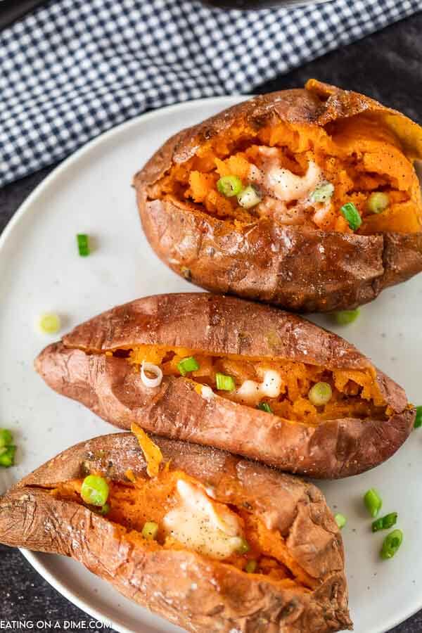 Cooked Sweet Potatoes on a white plate topped with butter and green onions