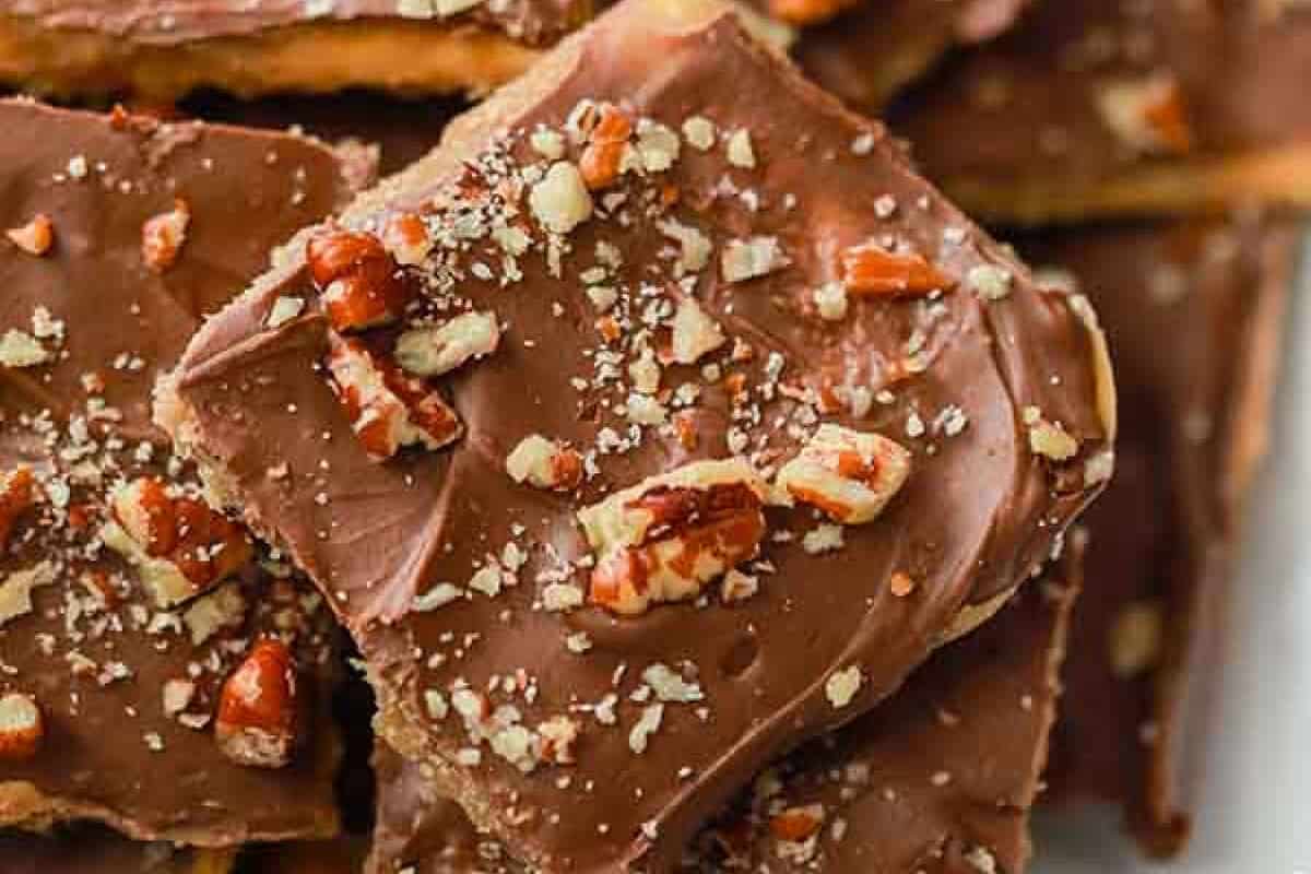 This Saltine Cracker Toffee is easy to make and sometimes called Christmas crack. This Saltine Cracker Toffee recipe is a favorite and is perfect for the holidays. Everyone will devour this toffee recipe! #eatingonadime #dessertrecipes #toffeerecipes Close-up of Saltine Cracker Toffee bars topped with a layer of chocolate and sprinkled with chopped pecans, stacked on top of each other.