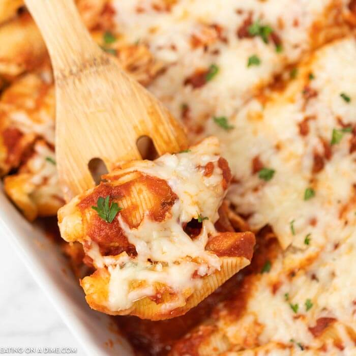 A pan full of stuffed shells and a spatula lifting 2 of the shells out of the pan. 