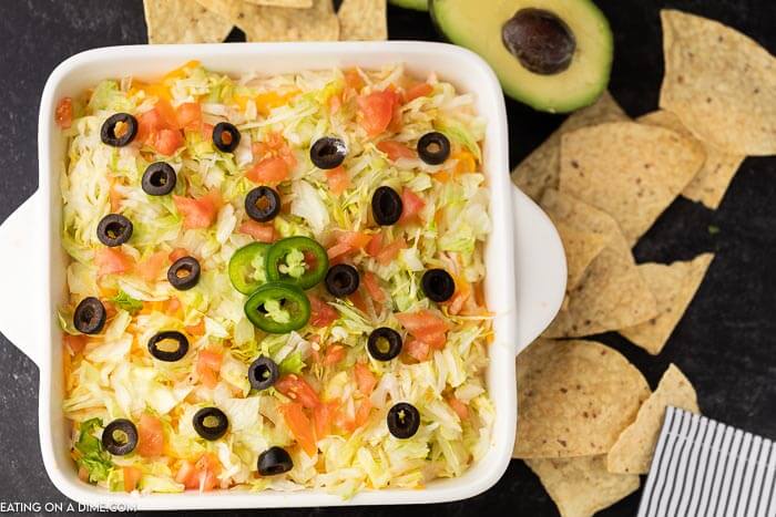 Close up image of Taco Dip in a 8x8 white dish with chips and avocado beside it. 