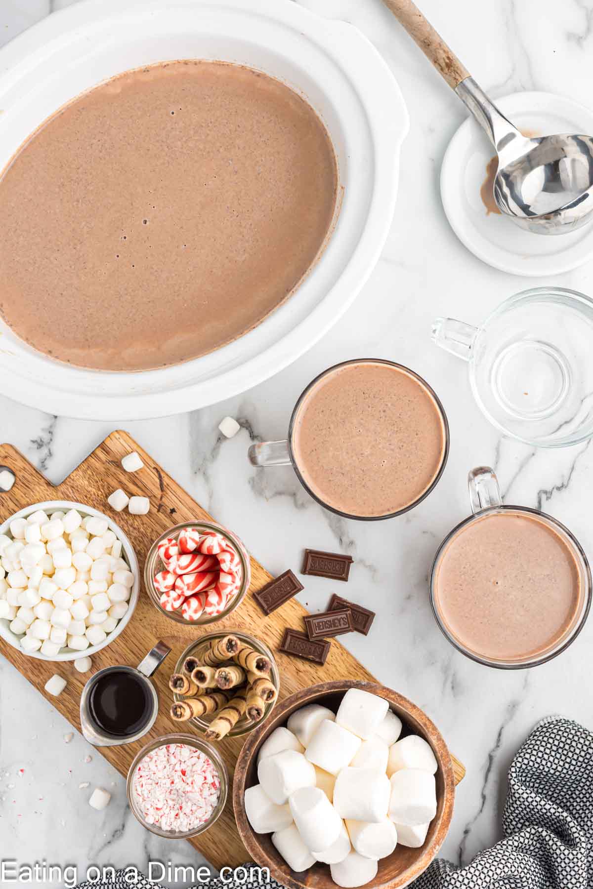 Hot chocolate in a slow cooker with a table with all the toppings