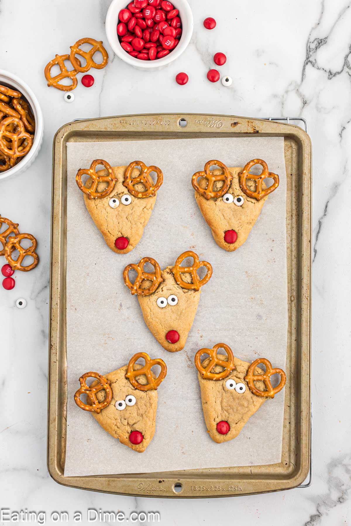 Top the cooked peanut butter cookies with pretzels, candy eyes and red M&M