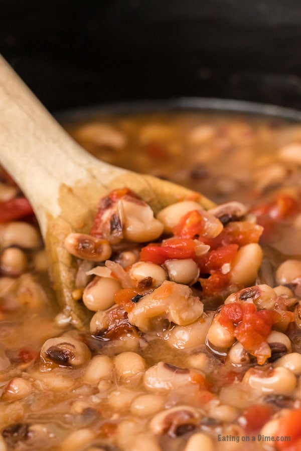 Black eyed peas in the crock pot with a wooden spoon