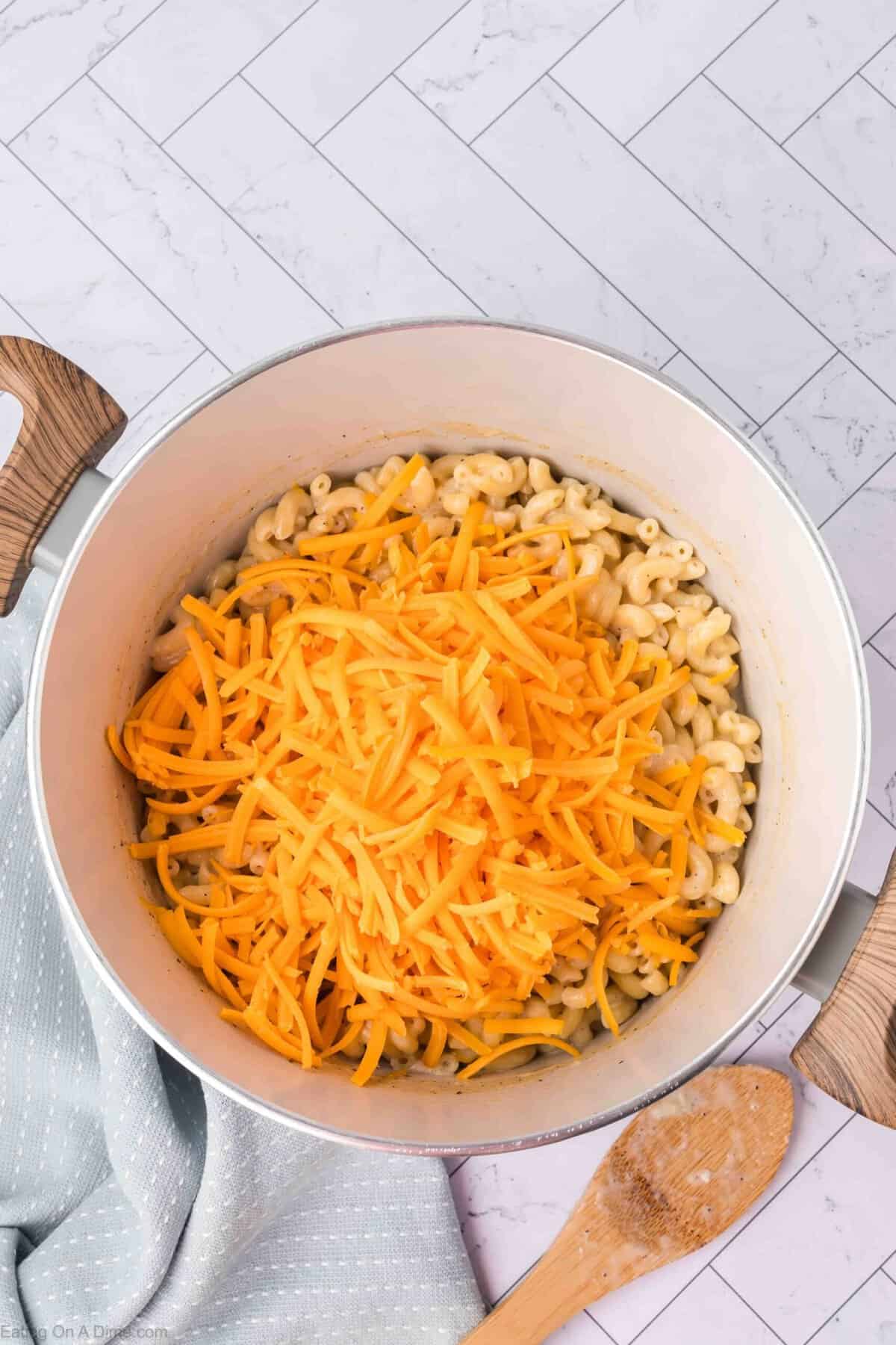A large pot filled with cooked macaroni noodles topped with a generous amount of shredded cheddar cheese.