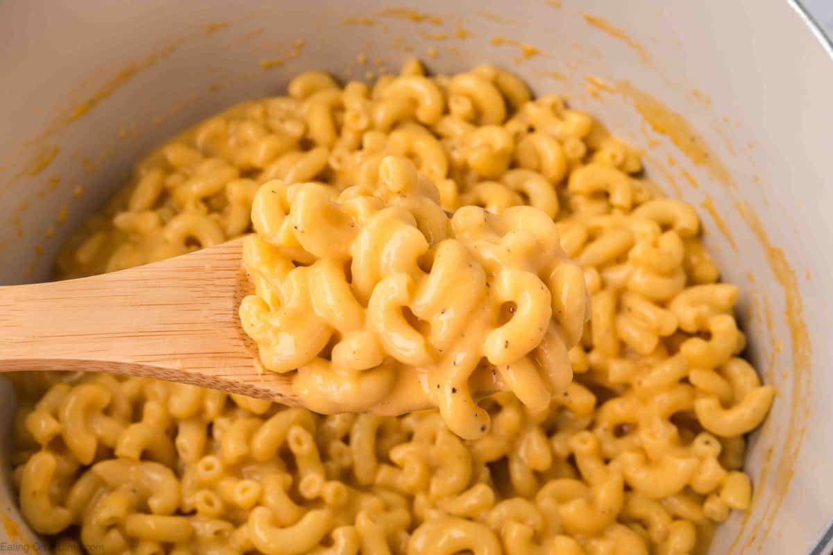 Macaroni and cheese in a large pot with a serving on a wooden spoon.