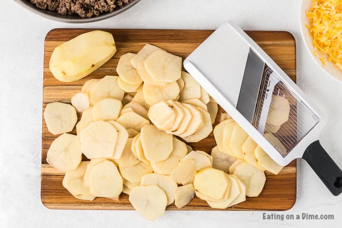 Slice potatoes on a cutting board with a mandoline slicer