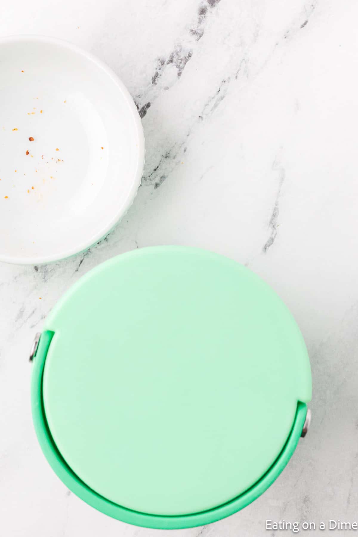 Insulated container with the lid on top with a empty white bowl on the side