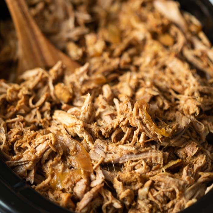 A large spoon scooping pulled pork out a crock pot.  