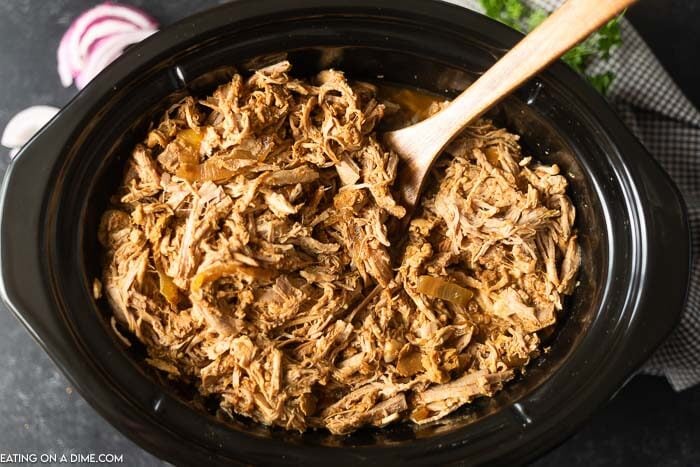 BBQ pulled pork in a black crock pot with a wooden spoon in it 