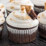 Chocolate cupcakes topped with toasted swirled marshmallow frosting, garnished with graham cracker and chocolate squares for the perfect s'mores cupcake recipe, all beautifully arranged on a dark wooden surface.