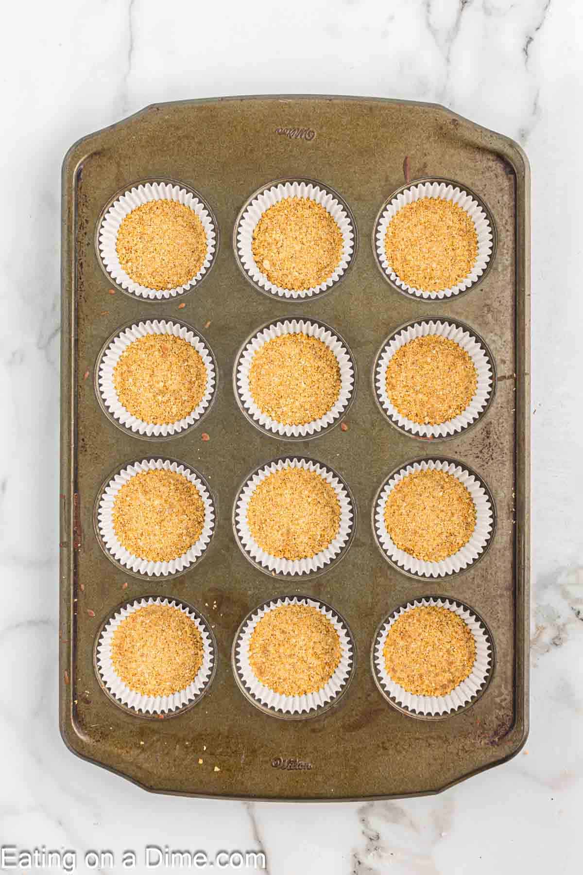 Pressing the graham cracker crumbs into the cupcake liners