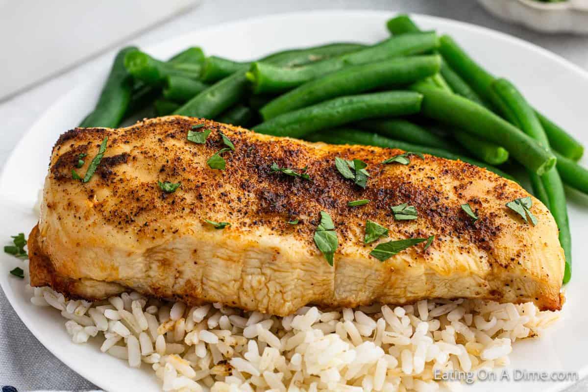 Chicken breast on rice on a plate with a side of fresh green beans