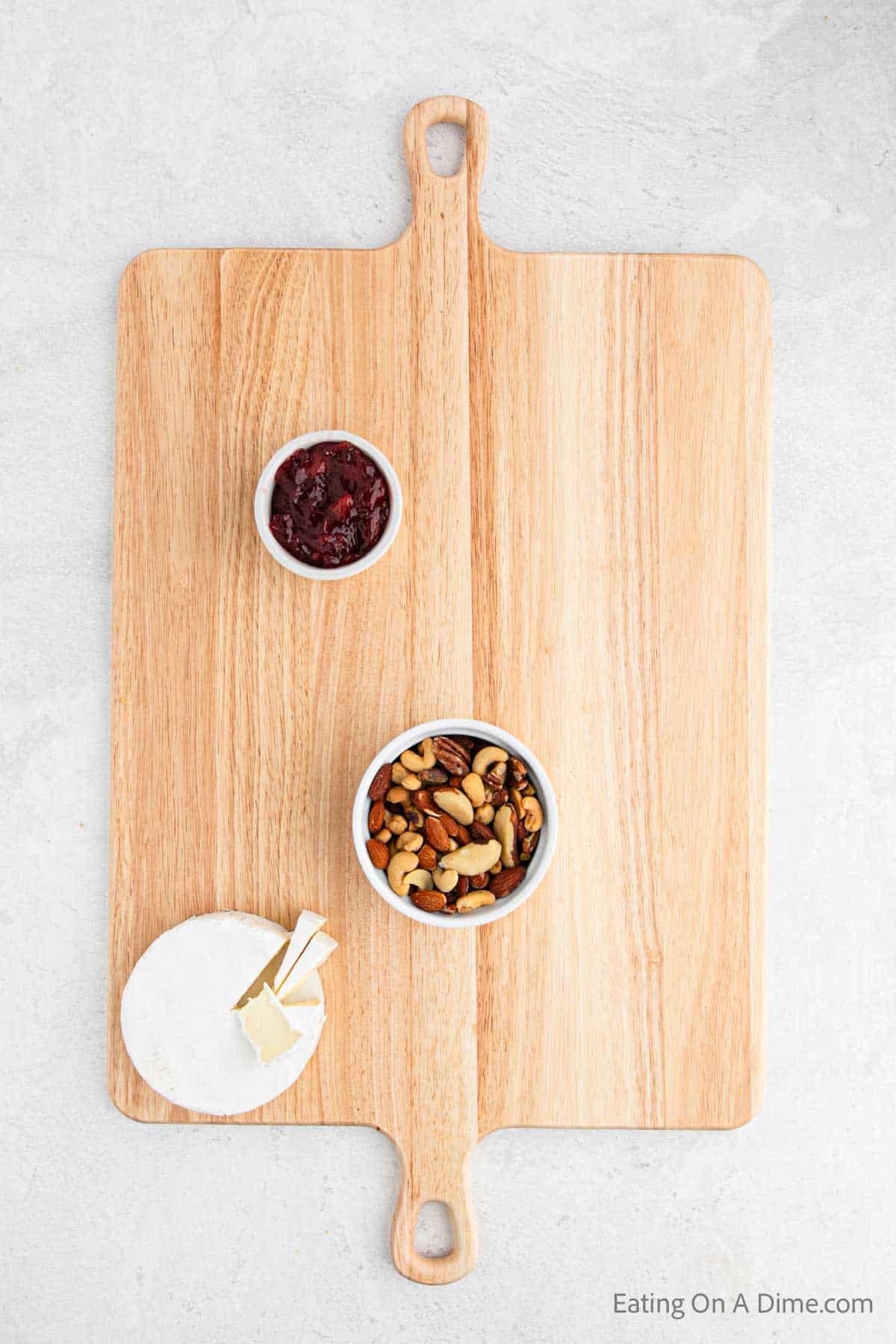 Place bowl of nuts, cheese and jam on the board