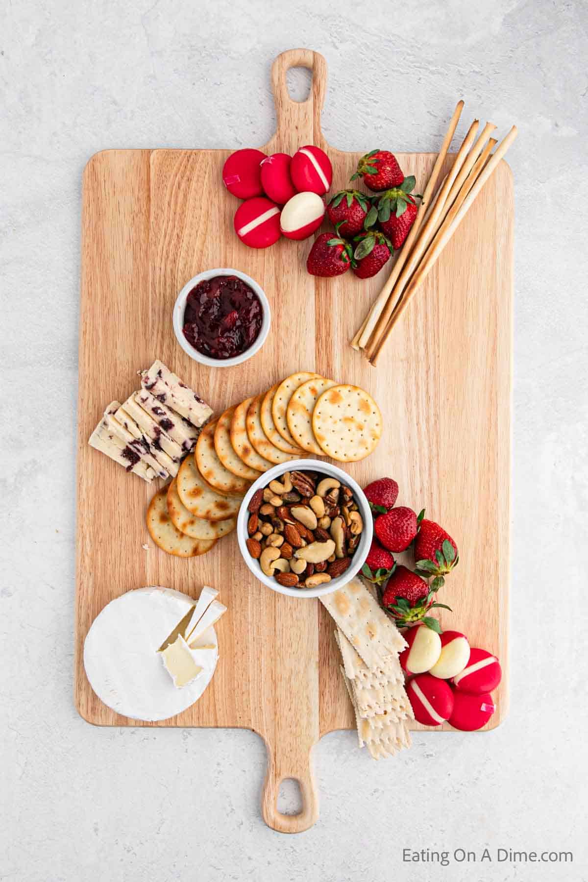Placing cheese, crackers, fruit and nuts on the board