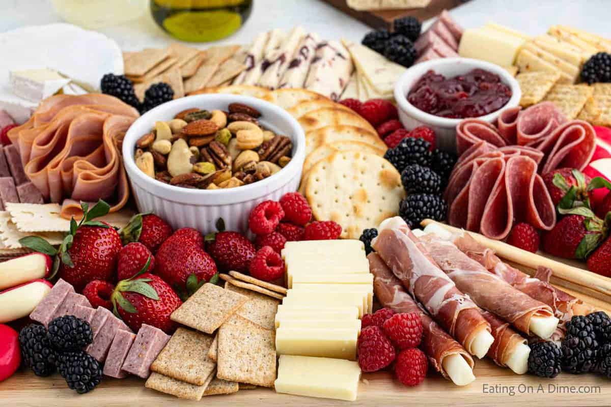 Learn how to make an easy Charcuterie board for your next party and totally impress your guests. You will be pleasantly surprised how simple it is to make. We have simple ideas to build a DIY charcuterie board everyone will love even the kids. These ideas are perfect for brunch, Christmas, 4th of July and more. #eatingonadime #howtomakeaCharcuterieboard Charcuterie Board topped with fresh fruit, crackers, meats and small bowls of nuts and spreads