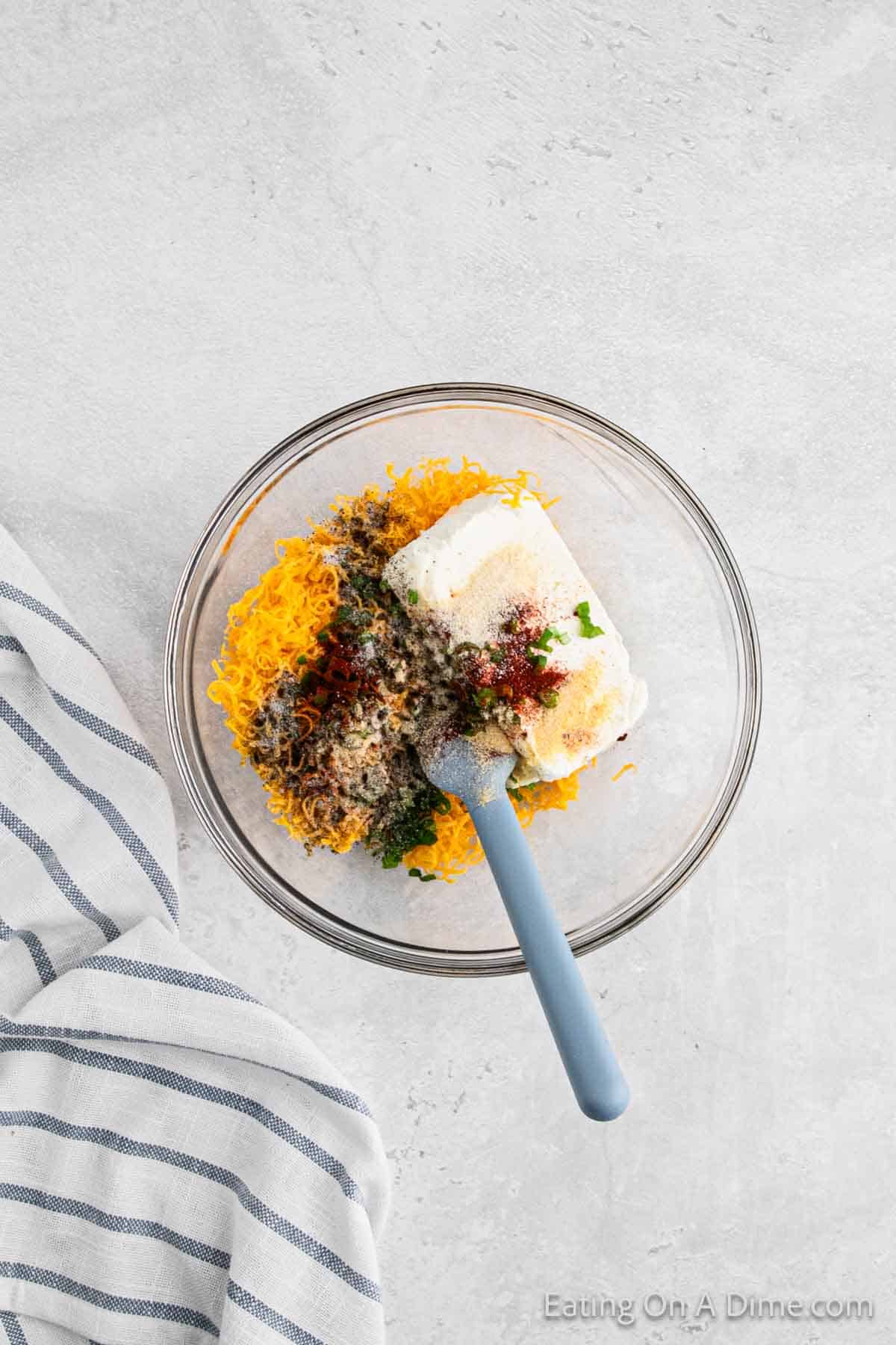 Combining the cream cheese, cheese, spices and chopped green onions in a bowl with a blue spatula