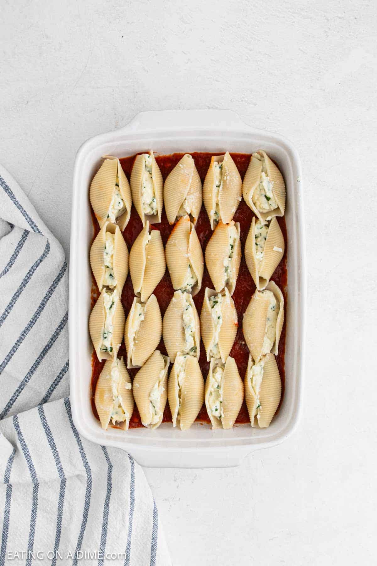 Uncooked stuffed pasta shells in a baking dish with marinara sauce on the bottom.