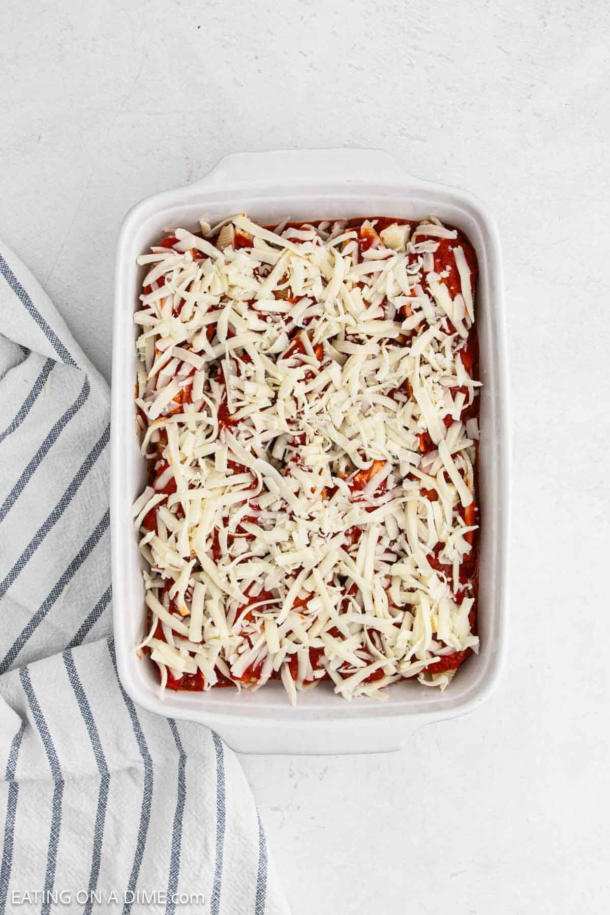 Shredded cheese and sauce topped the stuffed shells in a baking dish ready to bake.