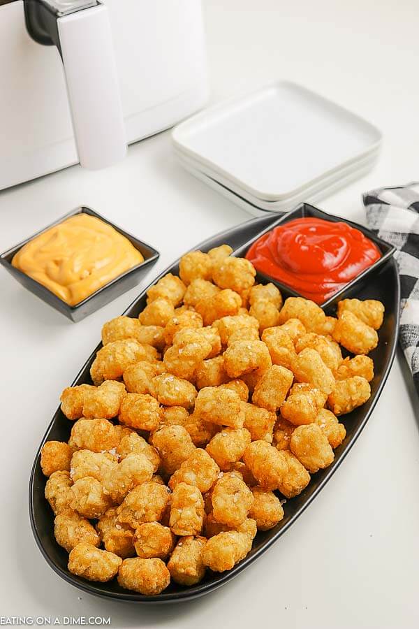 Close up image of tator tots witha  side of cheese sauce and ketchup. 