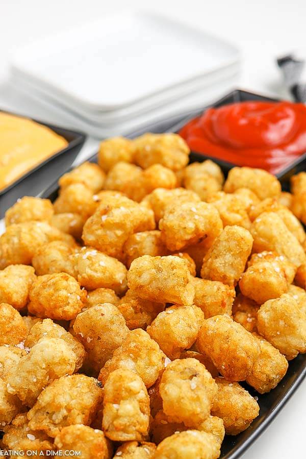 Close up image of tator tots on a platter with a side of cheese sauce and ketchup.
