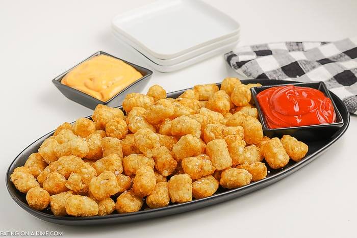 Close up image of a platter of tator tots with a side of cheese and ketchup. 