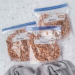 Three labeled resealable plastic bags filled with cooked beans are arranged on a light countertop, showing how easy it is if you’re wondering: Can You Freeze Cooked Beans? Each bag is marked "Beans" with a date. A gray textured cloth sits nearby.