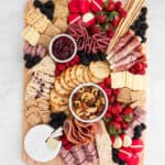 A simple Charcuterie board featuring assorted cheeses, crackers, cured meats, berries, nuts, breadsticks, and apple slices—all artfully arranged around two bowls of jam and mixed nuts.