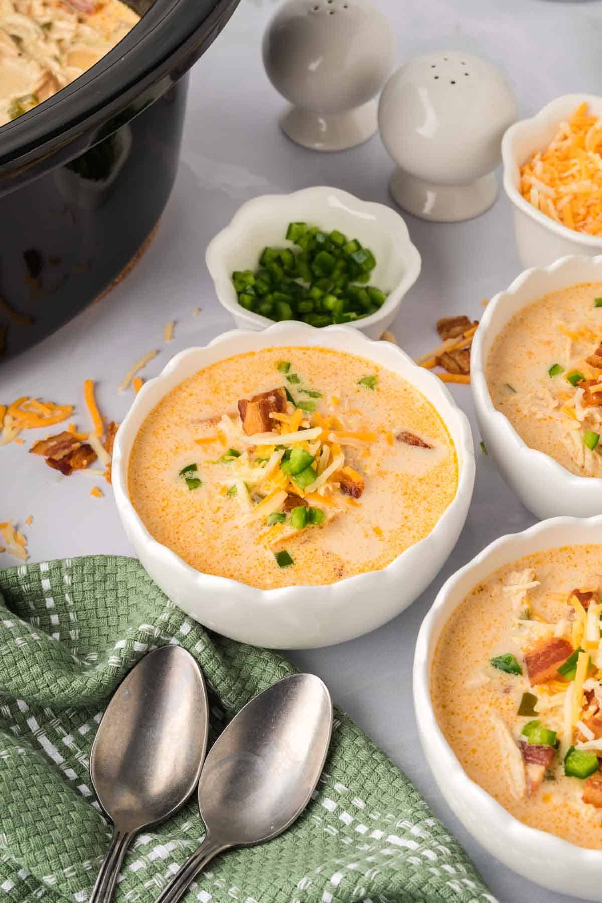 White bowls of Jalapeño Popper Chicken Soup topped with shredded cheese, diced jalapenos and bacon