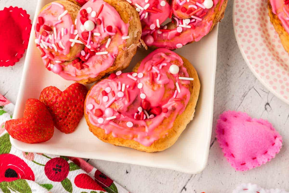 Heart Shaped Cinnamon Rolls on a white platter topped with pink frosting and sprinkles