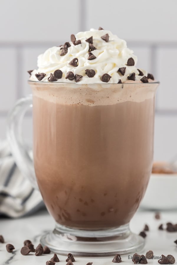 Clear mug with hot cocoa topped with whipped cream and chocolate chips. 