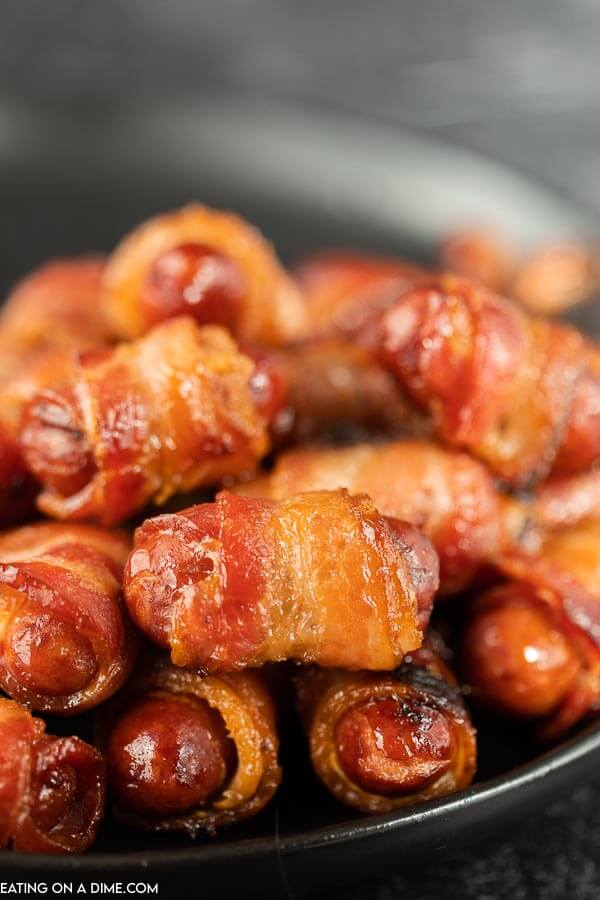 Close up image of bacon wrapped lil smokies on a black plate.