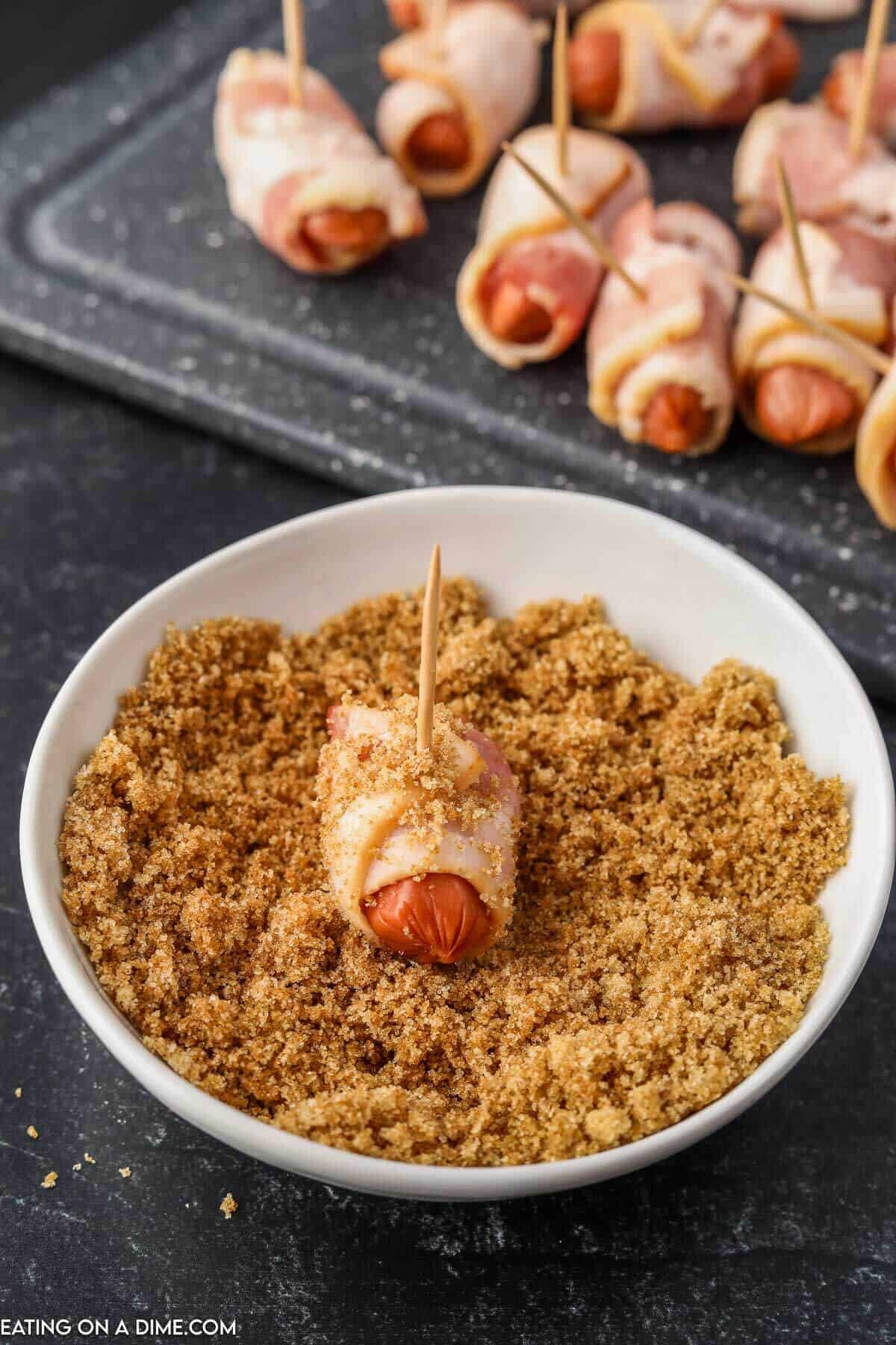 Dipping bacon wrapped smokies into the brown sugar mixture