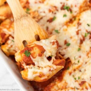 Stuffed Shells in a baking dish topped with melted cheese with a serving on a wooden spoon.