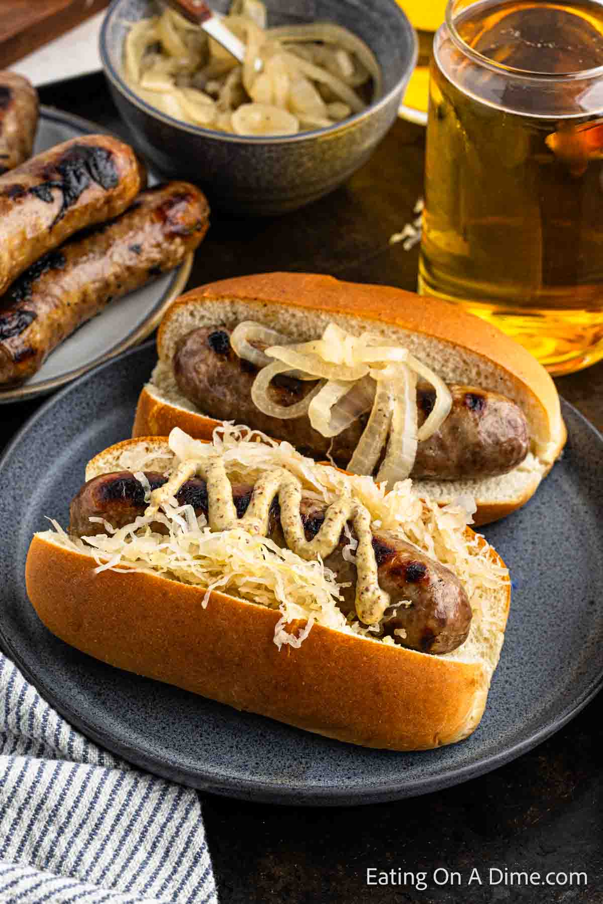 Grilled Brats  in buns on a plate topped with grilled onions and sauerkraut